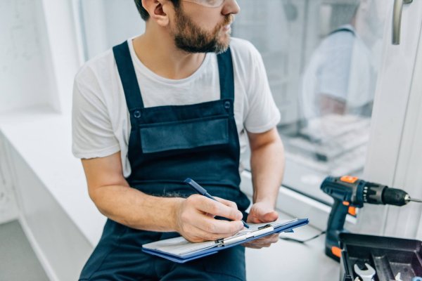 partial view of male handyman writing in clipboard and checking window.